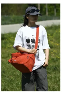 Vue détaillée d'un grand sac à bandoulière orange en tissu Oxford porté par un mannequin asiatique