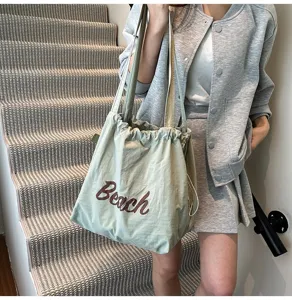 Detalle de estilo de vida de un bolso tote de nailon verde salvia con estampado de Beach