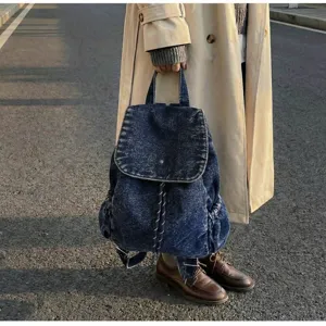 Close-up view of vintage denim drawstring backpack held by person in trench coat outdoors