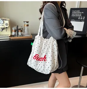 Primer plano del bolso hobo blanco con lunares y texto Beach rojo llevado por una modelo