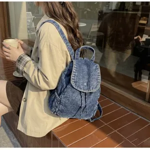Vintage blue washed denim backpack with drawstring closure shown on shoulder in a cafe