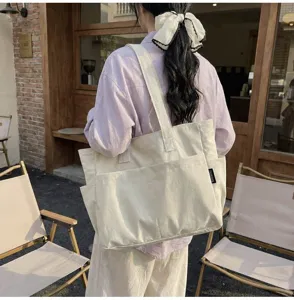 Modell mit einer großen minimalistischen beigen Canvas-Tasche im Außenbereich eines Cafés