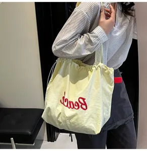 Modelo luciendo un gran bolso tote crema con bordado rojo Beach en una escena cotidiana