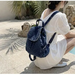 Vintage dark wash denim backpack with drawstring and flap closure worn by a model outdoors