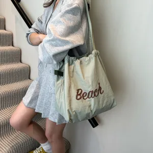 Bolso tote grande verde salvia con letras Beach llevado por modelo en escaleras