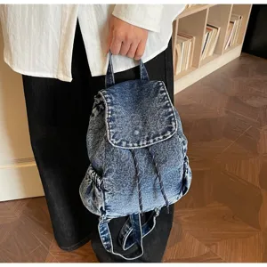 Lifestyle shot of a vintage-style blue denim backpack with a drawstring closure.