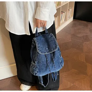 Close-up of a vintage denim drawstring backpack held in a cozy home library setting