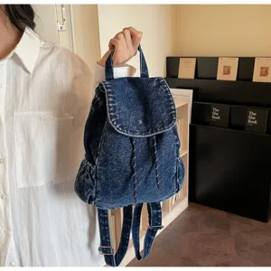 Close-up of a vintage blue denim backpack with drawstring closure held by a person in a white shirt.