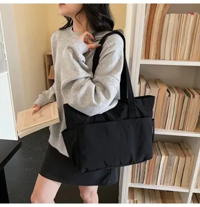 Modell mit einer minimalistischen schwarzen Canvas-Tragetasche in einer Bibliothek.
