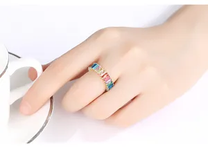 Primer plano de un anillo de circonita arcoíris en un dedo junto a una taza blanca.