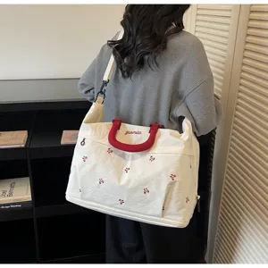 Stylish large white travel bag with red handles and embroidered bow patterns worn by a model