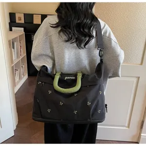 Rear view of a stylish black travel bag with green handles and embroidery details.