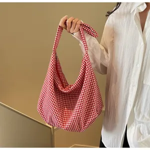 Detail shot of a red and white checkered nylon hobo bag held by a person in a white shirt