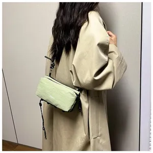Detail einer stilvollen hellgrünen Outdoor-Tasche über einem beigen Trenchcoat getragen