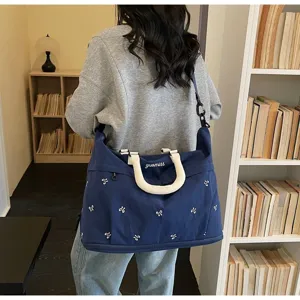 Woman carrying a large navy blue travel bag with bow patterns in a cozy room setting
