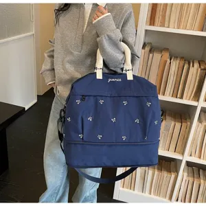 Large blue travel bag with embroidery carried by a model in a lifestyle setting