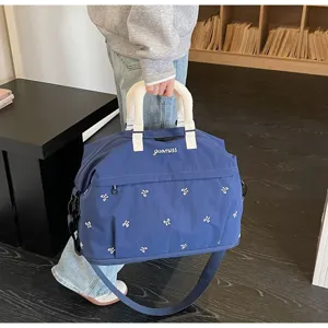 Detailed view of the large blue travel bag being carried, showing embroidery and handle.