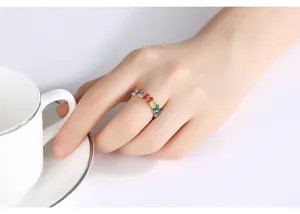 Close-up van een kleurrijke ring met zirkonia gedragen aan de vinger naast een witte kop