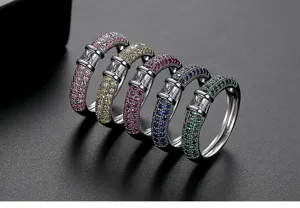 Primer plano de cinco anillos de latón con circonitas de colores sobre fondo oscuro elegante
