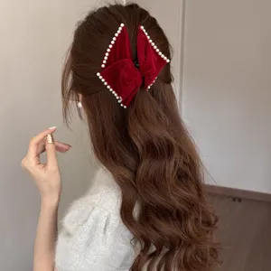 Red velvet bow hair clip with white pearl edges worn by a woman with wavy brown hair.