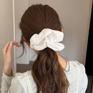 Dettaglio di un elastico per capelli in tessuto bianco a pois su capelli castani