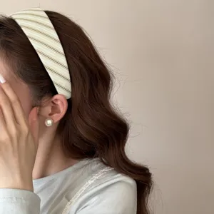 Gros plan d'un large bandeau rayé crème sur des cheveux bruns ondulés au style chic