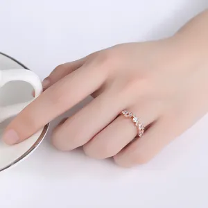 Elegante anillo de oro rosa con circonitas cúbicas en la mano junto a una taza de café blanca