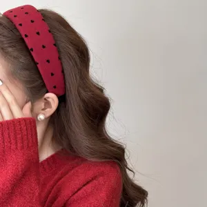 Vue détaillée d'un serre-tête en velours rouge à pois coeurs noirs sur cheveux bruns.