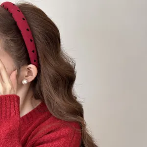 Close-up detail of an elegant red wide-brim headband featuring black heart patterns on a model
