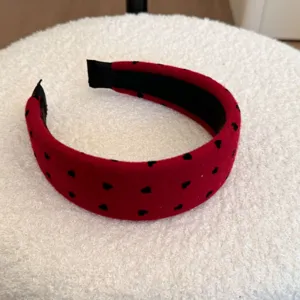 Vue détaillée d'un serre-tête en velours rouge avec de jolis motifs de cœurs noirs