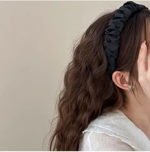 Vista detallada de una diadema plisada negra con patrones de lazos sobre el cabello