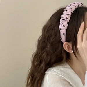 Diadema de tela plisada rosa con estampados de lazos negros para un look dulce.