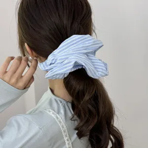 Close-up detail of a light blue striped fabric scrunchie styled on a low ponytail