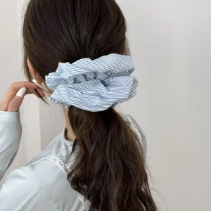 Close-up of a blue and white striped fabric scrunchie worn on a low ponytail