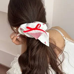 Close-up of a white cherry print scrunchie with red bow and lace detail on a ponytail