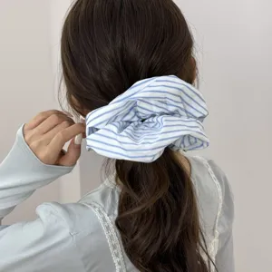 Close-up detail of a dreamy blue and white striped scrunchie styling wavy brown hair