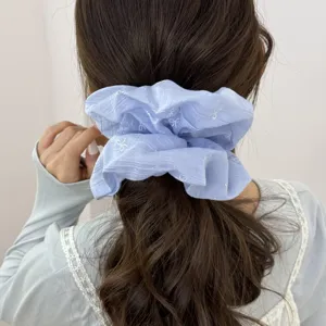 Détail d'un chouchou bleu clair à motif de nœud coiffé dans une queue de cheval ondulée