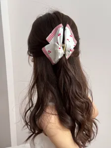 Close-up detail of a sweet white hair claw clip with cherry print and a gingham bow decoration