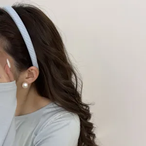 Close-up of a stylish blue striped fabric headband and a large elegant pearl earring.