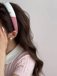 Close-up view of a sweet white headband with cherry and red gingham patterns on a model