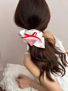 Detail view of a sweet white scrunchie with cherry pattern and red bow hair tie