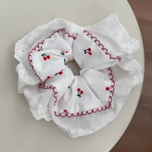 Detail view of the white lace scrunchie featuring a delicate cherry pattern and scalloped trim.