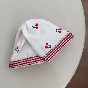 Detailed view of a sweet white fabric scrunchie featuring cherry prints and red checkered trim