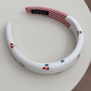 Detailed view of white padded headband featuring cute cherry prints and red checkered lining