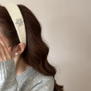 Macro detail view of an elegant cream plush headband with a shiny rhinestone snowflake.