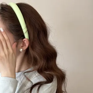 Gros plan d'un serre-tête rembourré vert clair porté sur des cheveux bruns ondulés