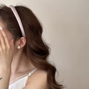 Détail de profil d'un élégant serre-tête rose clair à fleurs sur des cheveux ondulés.