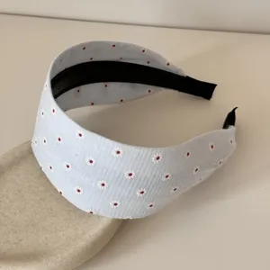 Dettaglio del cerchietto in tessuto azzurro con motivo floreale bianco su supporto.