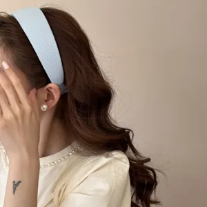 Close-up side view of a soft light blue padded headband worn on brown wavy hair