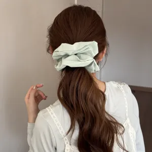 Vue arrière d'un modèle portant un chouchou géant en tissu vert clair dans une queue de cheval